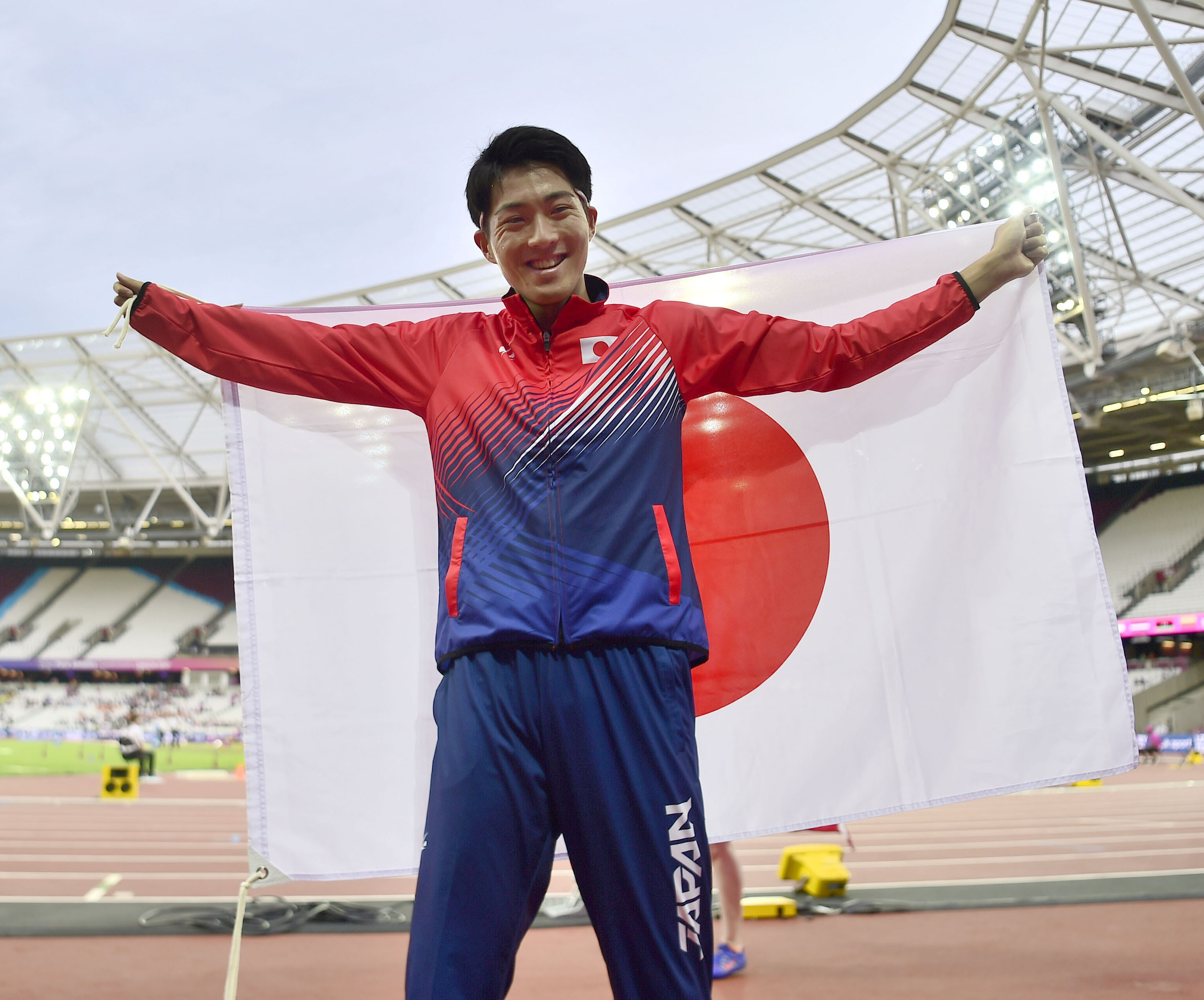 男子三段跳び(T47)で3位となり、日の丸を背に笑顔の芦田創=ロンドン(共同)